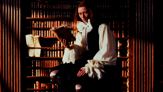 Orlando © Studio Canal Person in historischer Kleidung sitzt vor hohen Bücherregalen und hält ein geöffnetes Buch in der Hand