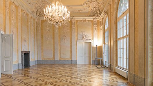Blick in einen mit Stuck verzierten Saal mit Kronleuchter im Schloss Schönhausen