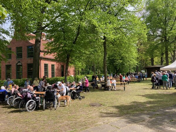 Veranstaltung am Jagdschloss Stern, Menschen sitzen bei sonnigem Wetter im Freien auf Bierzeltgarniuren, im Hintergrund das Jagdschloss