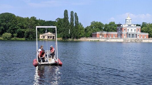 Helmholtz-Zentrum für Geoforschung nimmt Probebohrungen im Heiligen See vor, 3 Personwen auf einen Boot mit Bohrvorrichtung auf dem See, im Hintergrund Marmorpalais und Schlossküche