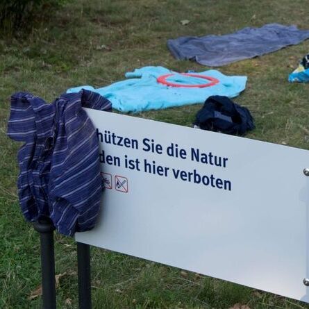 Neuer Garten im Sommer, über einem Schild „Schützen Sie die Natur. Baden ist hier verboten“ hängt Badekleidung zum Trocknen