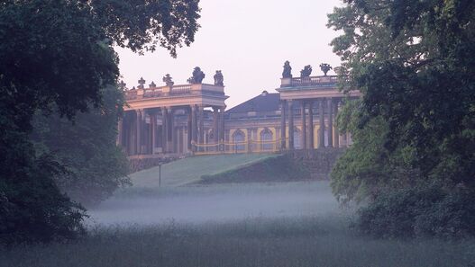 Schloss Sanssouci, Blick auf die Kolonnaden von der Straße aus über die Wiese mit Morgennebel