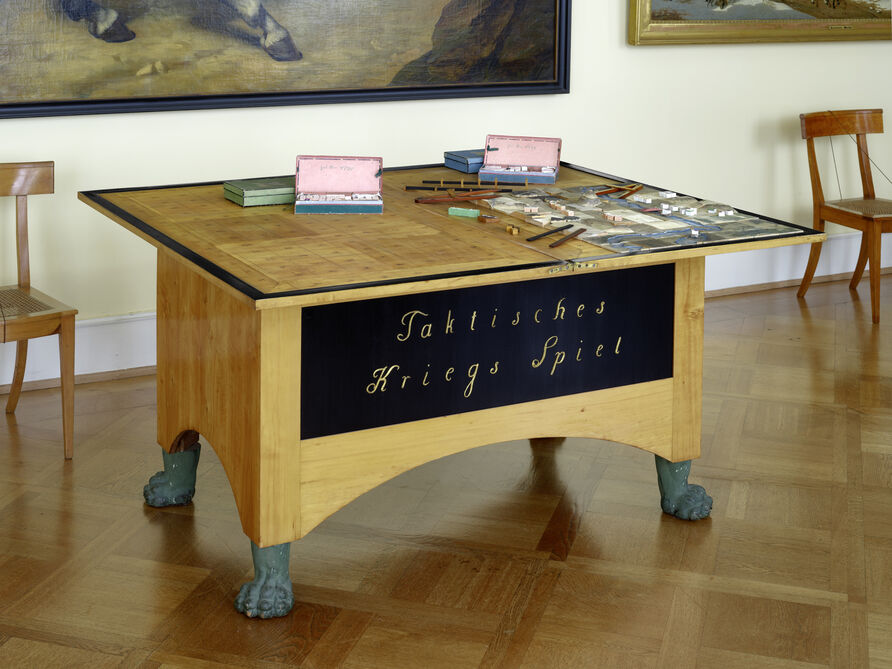 Domänen- und Kriegsrat Georg Leopold Baron von Reisswitz, Kommode „Taktisches Kriegs Spiel" für Friedrich Wilhelm III., 1812.  Das später weiter entwickelte Kriegsspiel befindet sich heute im Neuen Flügel des Schlosses Charlottenburg, im Raum 314. Was für die Besuchenden wie eine schlichte Kommode anmutet, verbirgt in seinem Inneren unbegrenzte Möglichkeiten an Kriegssimulationen.