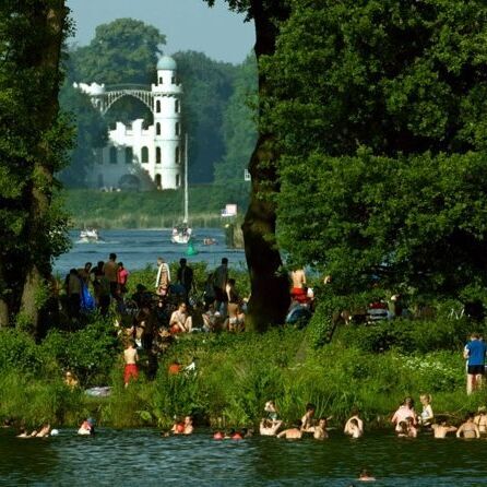 Neuer Garten im Sommer, Badende am See, im Hintergrund – eingerahmt durch Bäume – das Schloss Pfaueninsel